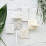 Stylish flat lay with marble tiles and lush green foliage for modern design inspiration.